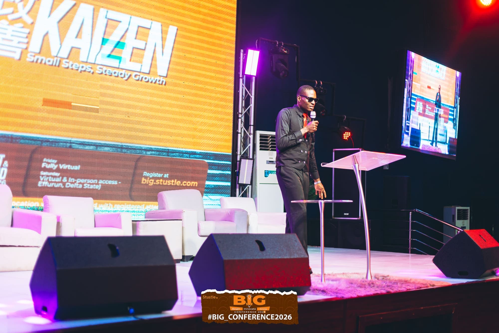 A speaker on stage in front of the Kaizen screen